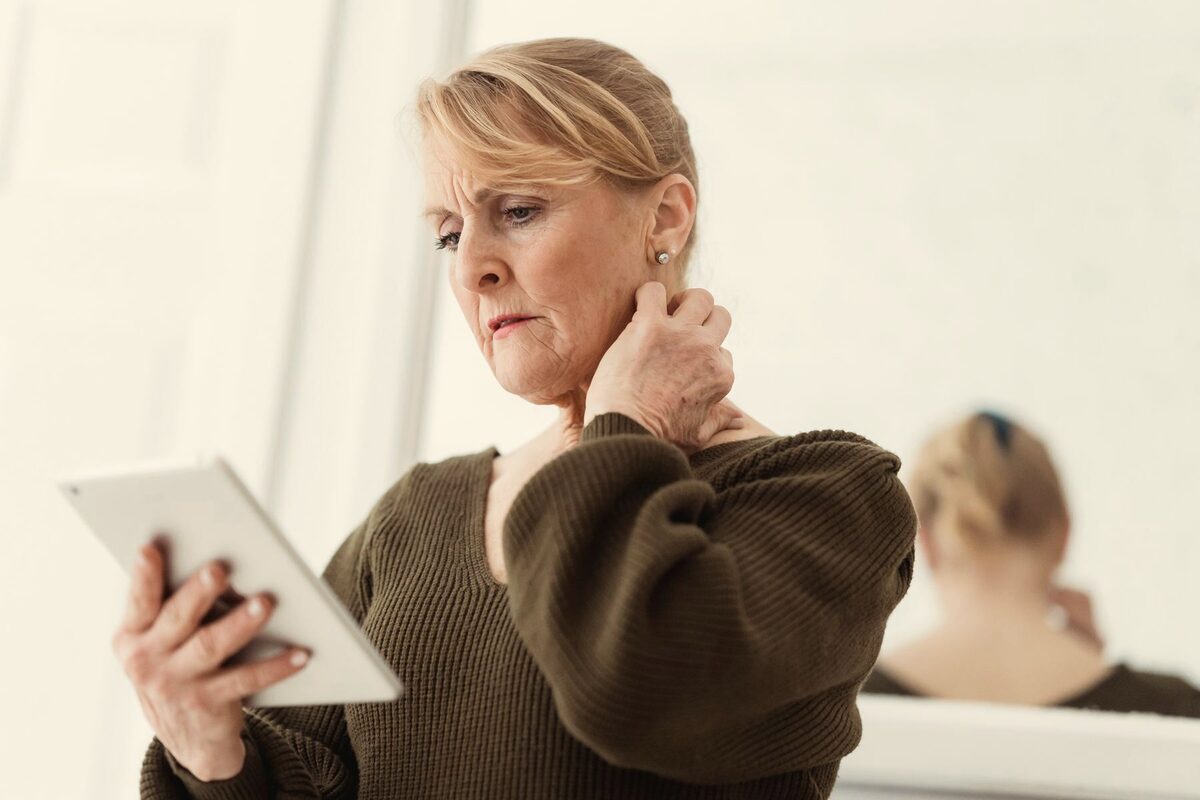 Une femme regarde une tablette, une main posée sur la nuque